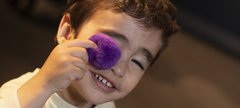 Small boy holds coloured ball up to his face 