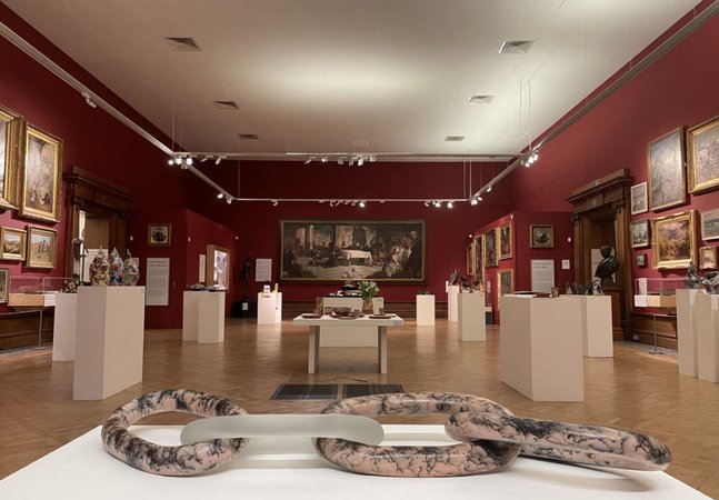 A display of glass and ceramic objects on white plinths in a gallery space.