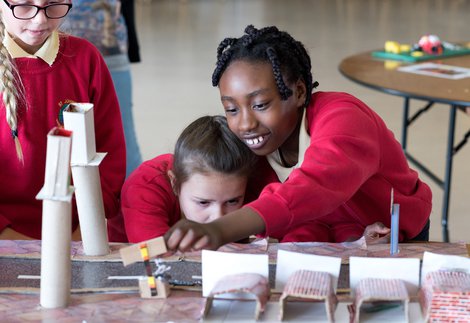 Two young school girls bend over an experiment smiling while a third looks on