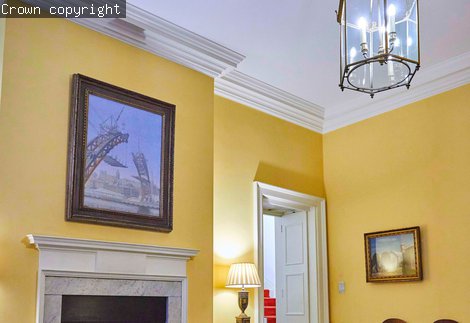 A painting of the building of the Tyne Bridge hangs above a fireplace. The walls are yellow and the ceiling is white.