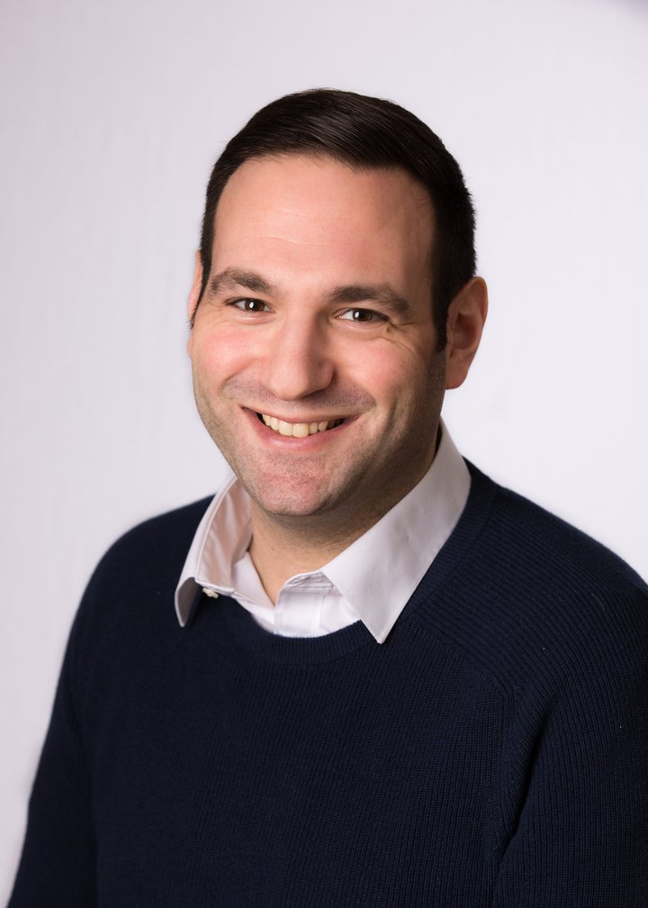 smiling brown haired man in dark jumper & white shirt 