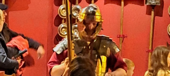 Roman solider holding a spear and shield in Shrine of the Standards talking to a young boy