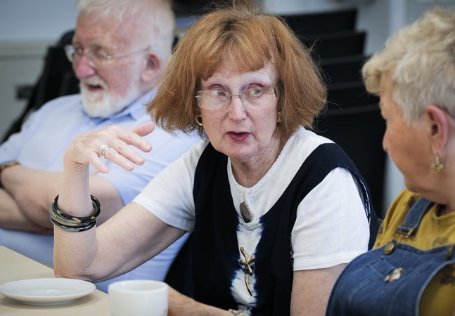 A photograph of three people conversing around a table.