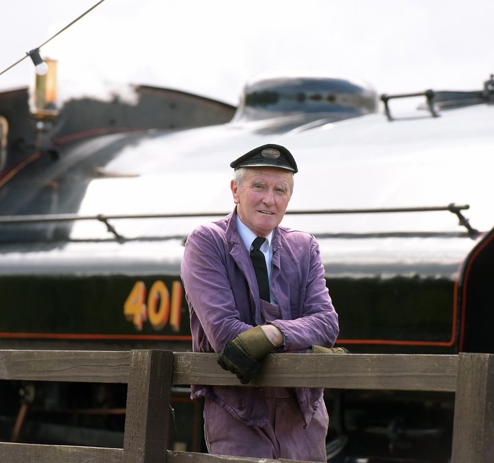 Man with cap in front of black steam locomotive