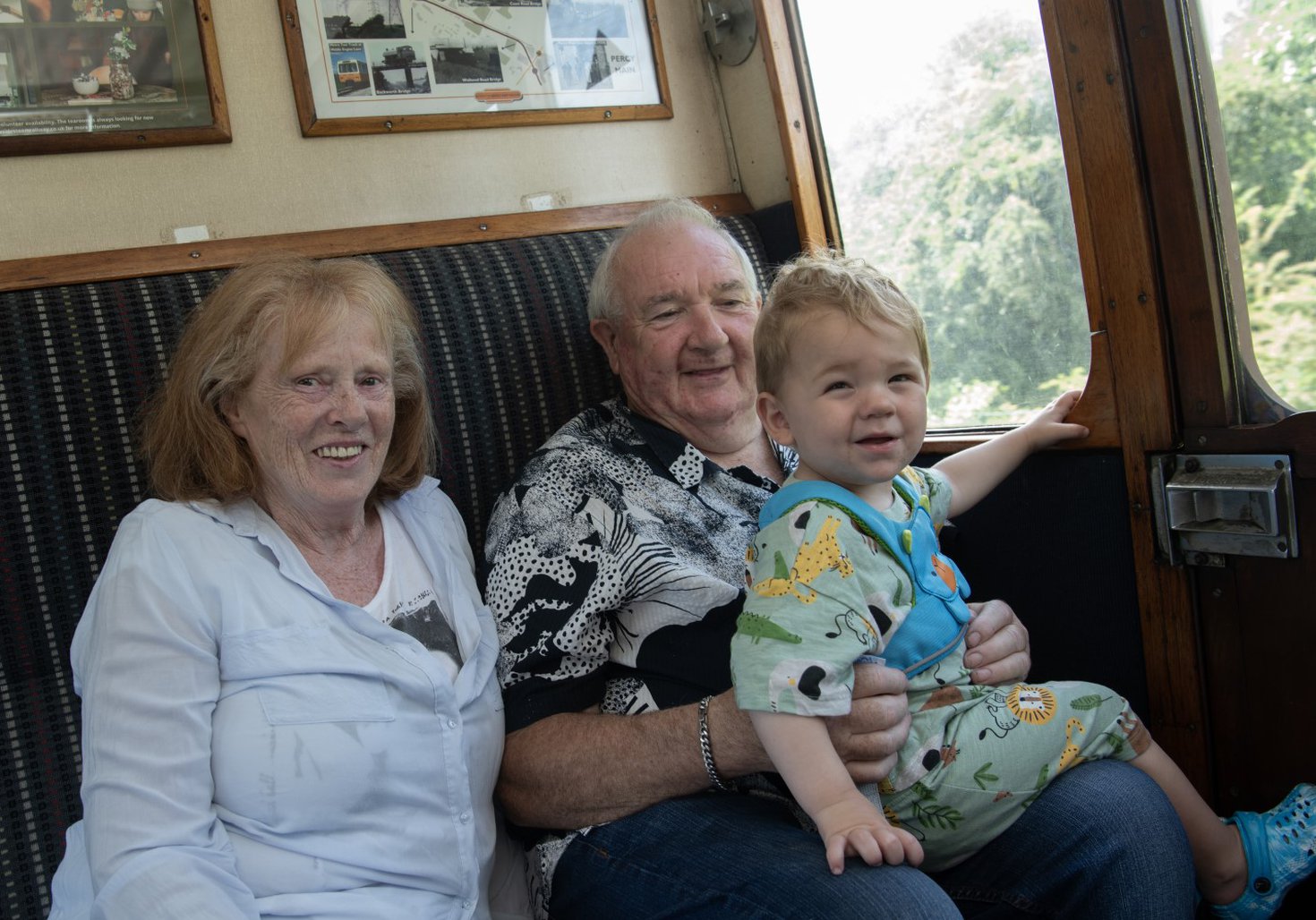 A family of three sit in a train carriage. They are smiling at the camera