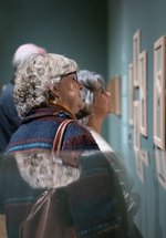 A woman looking at prints on a wall in a frame.