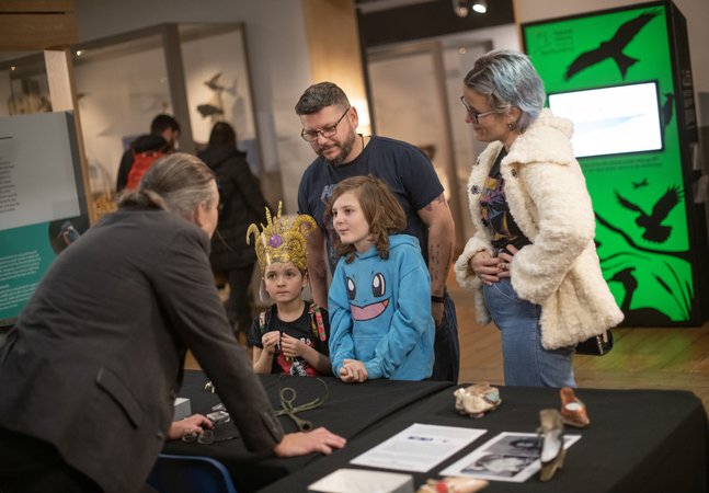 Two children and two adults are listening to a curator talk about museum objects.