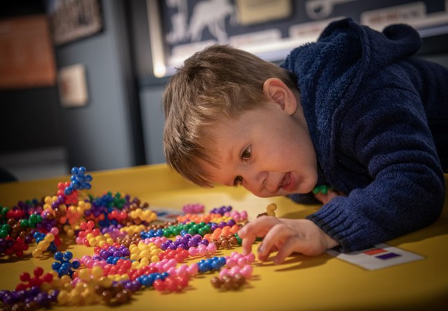 A child leans over a table and plays with a set of colourful  atom shaped toys