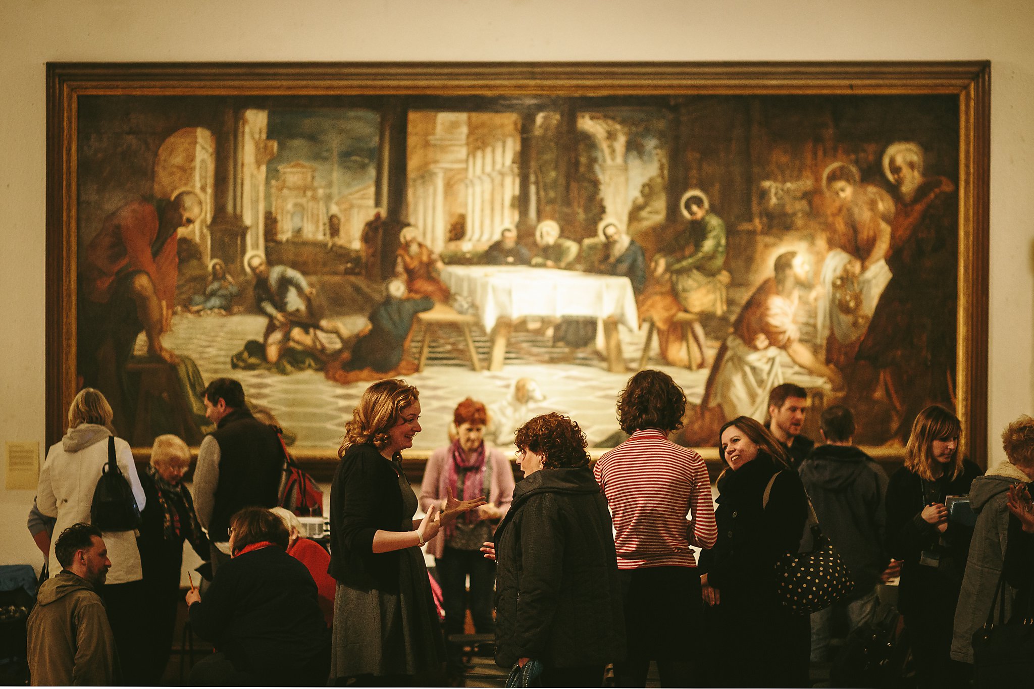 A group socialising in front of a large painting in a museum.