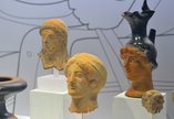 Four Ancient Greek artefacts showing feminine heads and faces. One item is a jug.