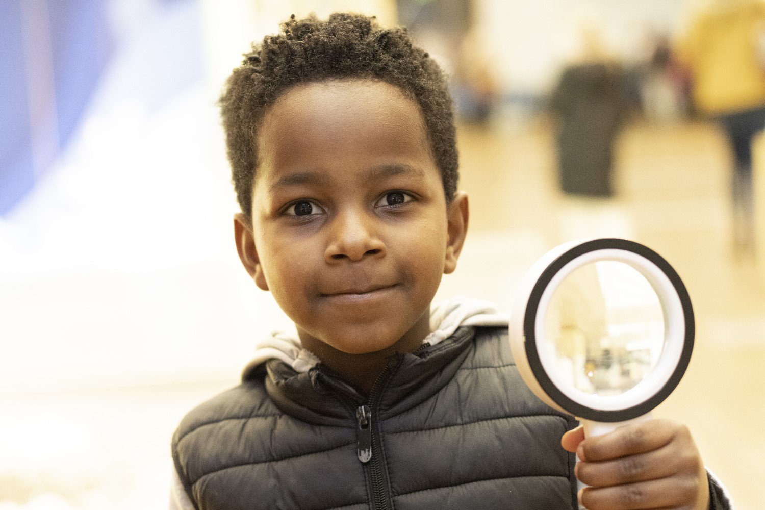 A child smiles at the camera, holding a magnifying glass. A child smiles at the camera, holding a magnifying glass.