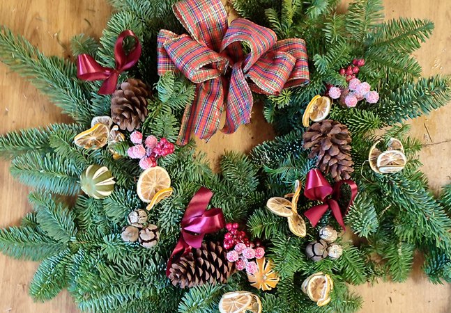 A photograph of a Christmas wreath decorated with dried oranges, pinecones, ribbons, and other decorations.