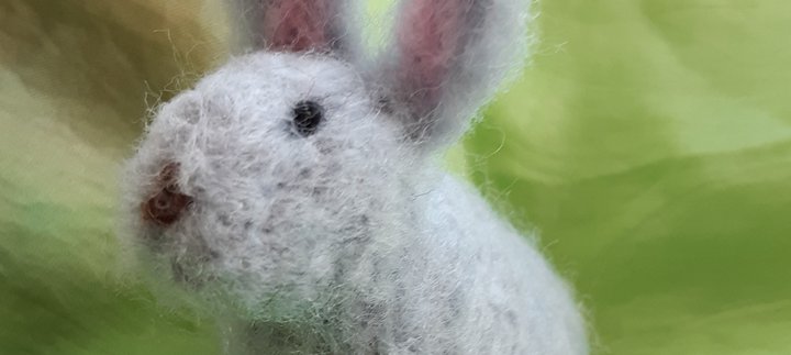 a needle felted bunny sitting on a green background