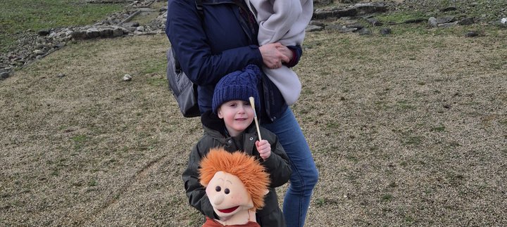 A woman holding a baby while a young child holds a soft toy on the fort site