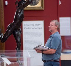 A person looking at a sculpture, the person is holding a notebook.