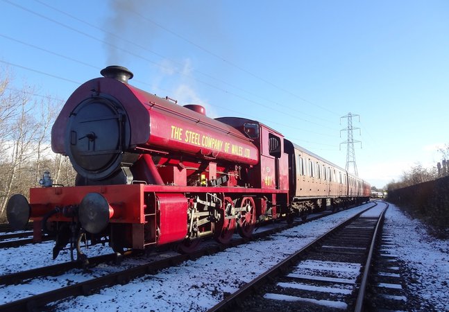 Red steam locomotive pulling passenger carriages on snow covered railway