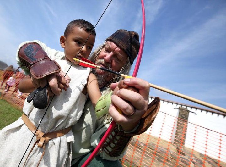 Man helping a young person to learn archery