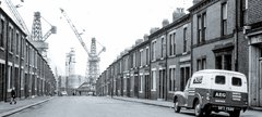 Black and white photo of street with terraced housing leading to shipbuilding yard and cranes