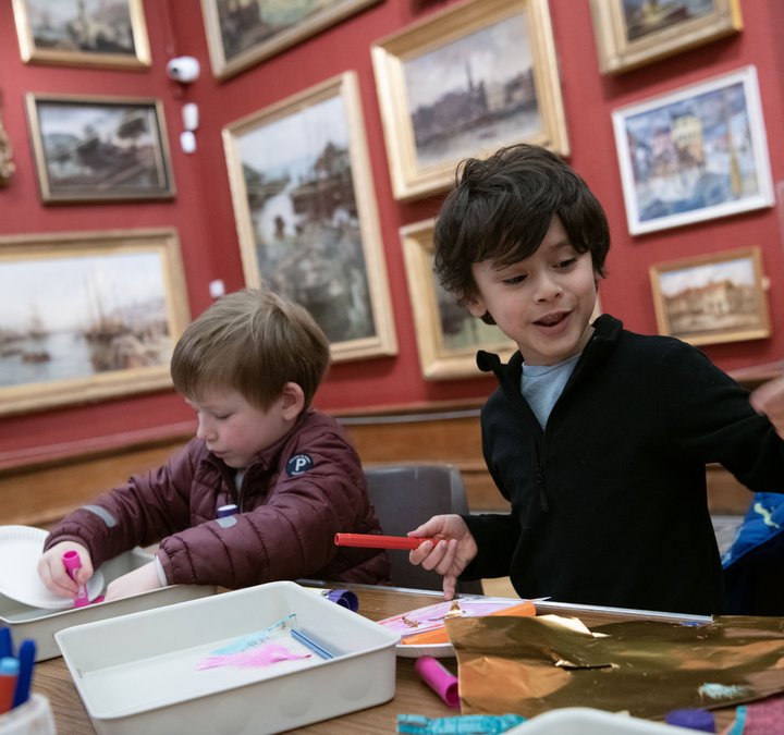 Two children sat at a table playing with craft materials in an art gallery