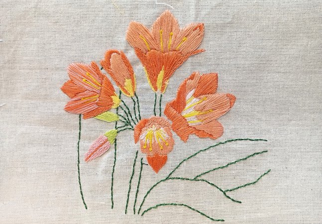 Orange, yellow and green embroidered flowers on pale fabric background 