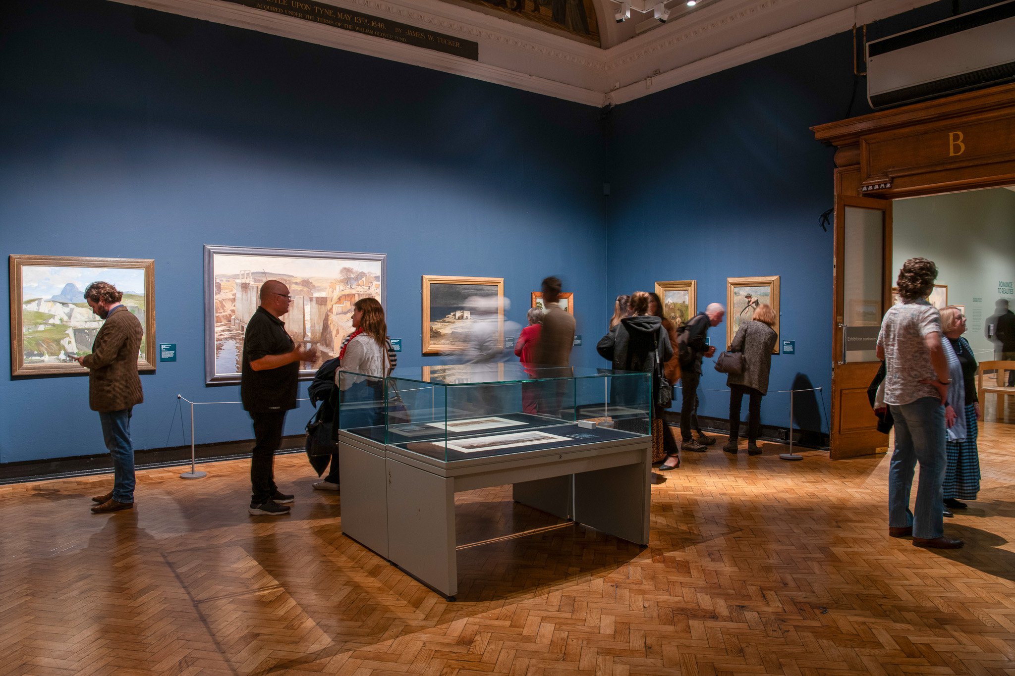 A busy art gallery filled with people looking at paintings on the walls 