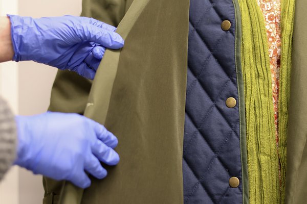 blue gloved hands peel back a lapel on a green coat
