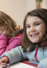 Two children sat at a table, one looks directly at the camera, grinning