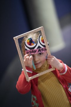 Portrait photo of young girl holding up an empty photo frame around her head.