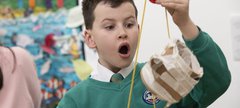 A child looks in awe at a homemade pulley system made of string and cardboard 