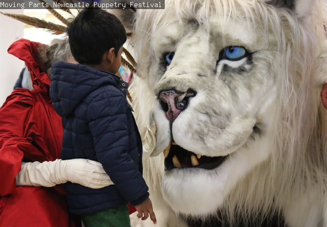 An adult and a child are looking at a large snow lion puppet