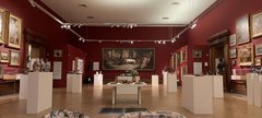 A display of glass and ceramic objects on white plinths in a gallery space.