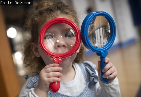 Small girl  charmingly squints through two magnifying glasses Toddler Takeover
