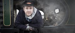 Man wearing railway cap with badge standing on the footplate of a steam engine