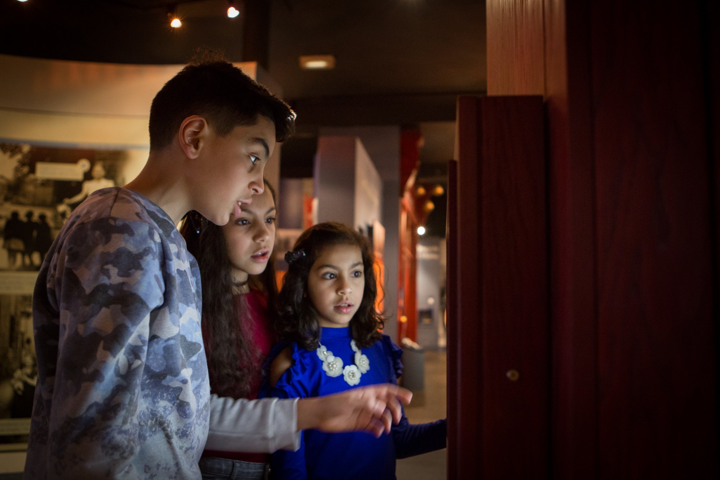 Three children look at a museum display case. Three children look at a museum display case.