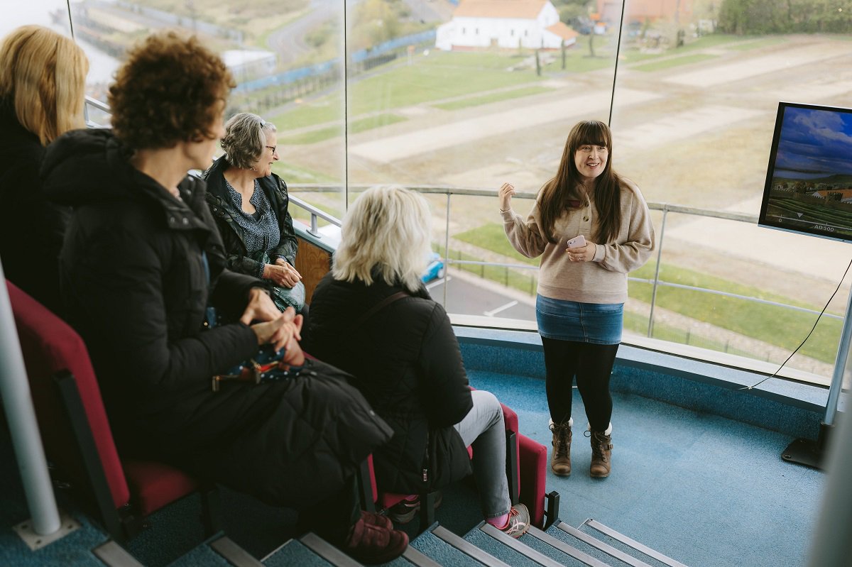 A person with long brown hair giving a talk to a small group of people. A person with long brown hair giving a talk to a small group of people.