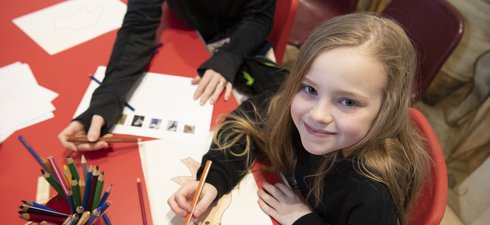 Young girl with long hair sitting at a table drawing with a colouring pencil