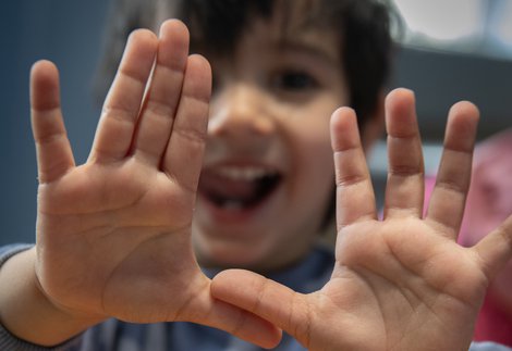 Little smiling boy holds up hands to camera