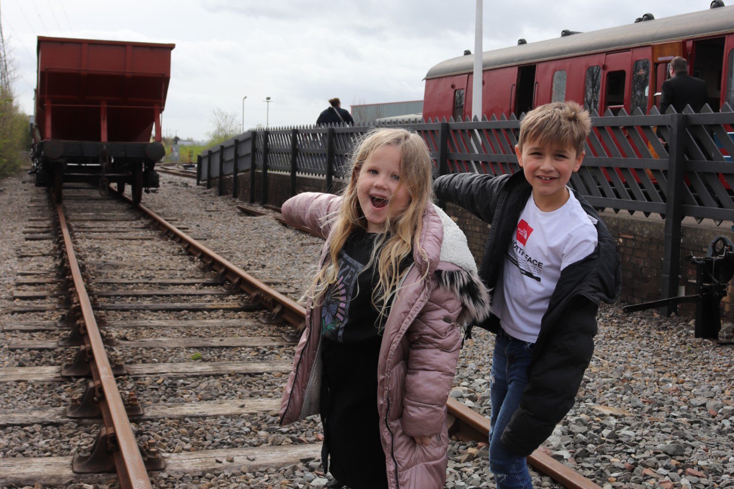 Two children stand on a railway track pointing at a freight. In the background is a passenger carriage