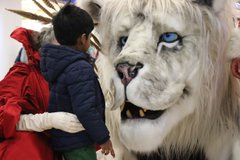 An adult and a child are looking at a large snow lion puppet