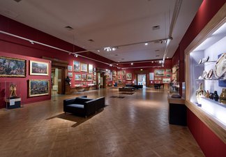 A photograph of the interior of the Shipley Art Gallery. The walls are red and there are many paintings on the walls in gold frames.