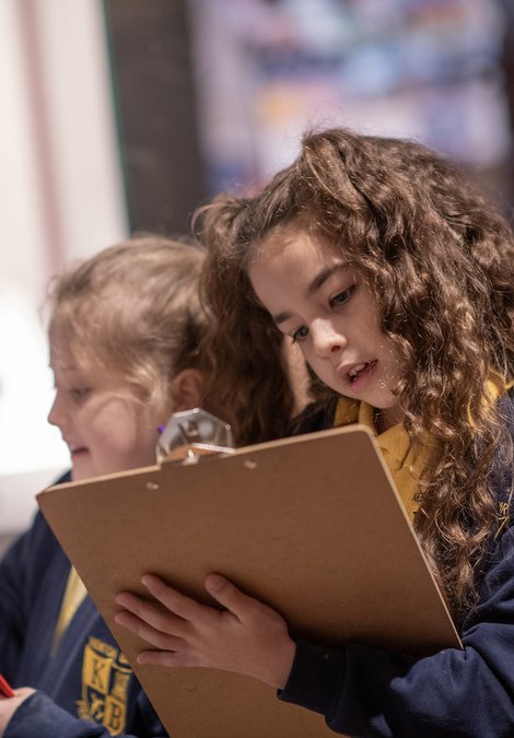 Two schoolchildren writing on clipboards in an art gallery