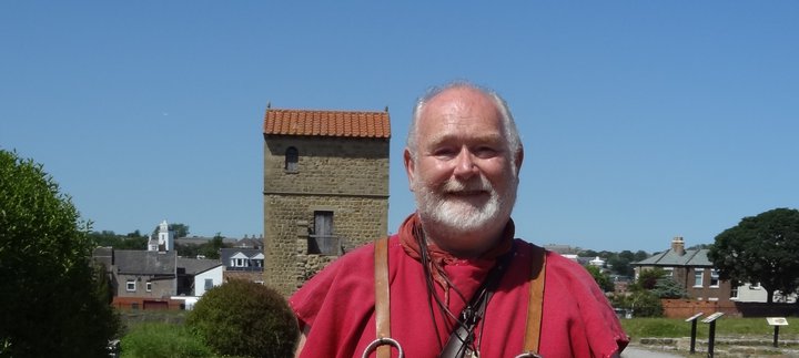 Man dressed in a red Roman style tunic holding a wooden staff