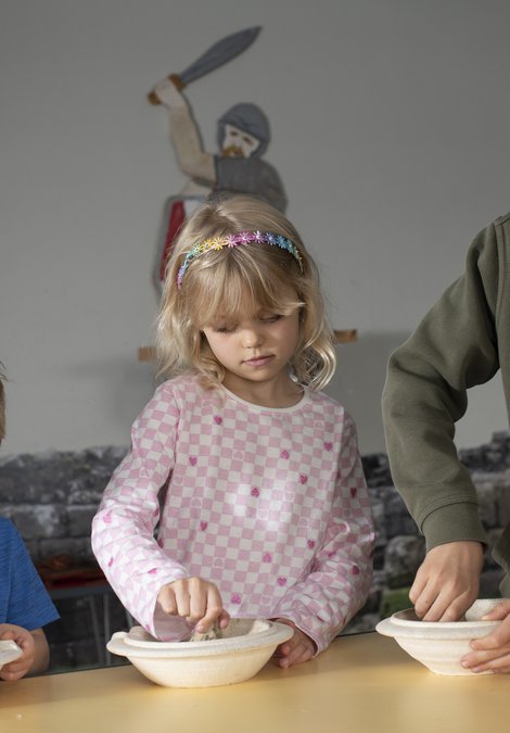 Three children grinding and mixing herbs with pestles and mortars