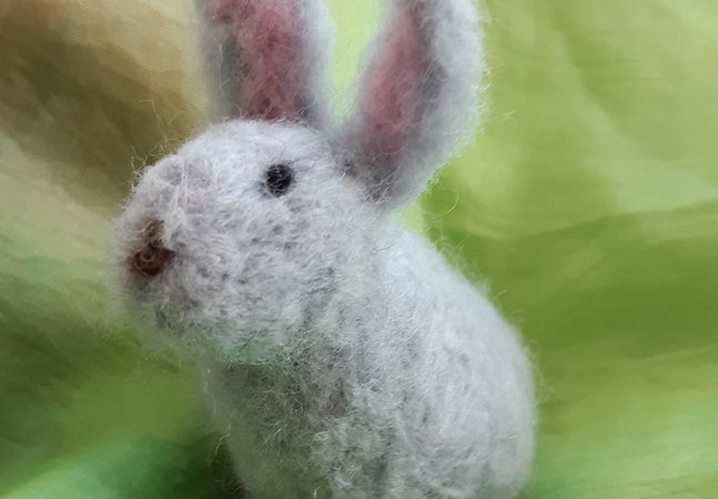 a needle felted bunny sitting on a green background