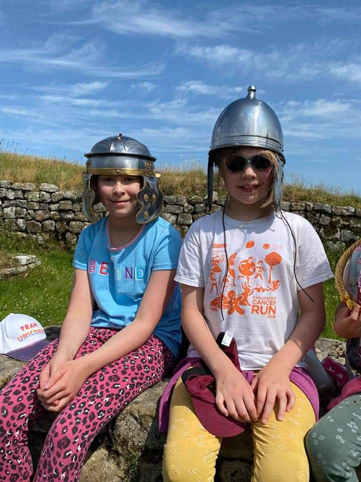 Two children sitting down and wearing replica Roman soldiers helmets