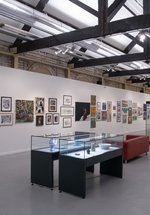 A gallery space with artworks on the walls and glass display cases filled with pottery and sculpture