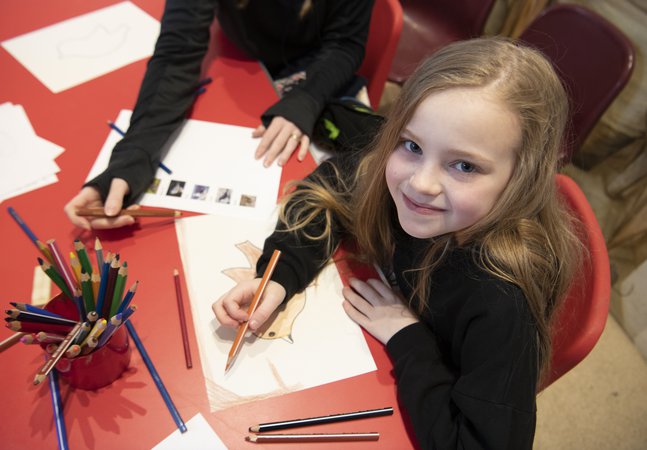 Girl sitting at a red table colouring in some paper