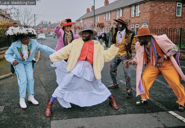 A photograph of five people in a circle dressed in colourful, formal outfits. 