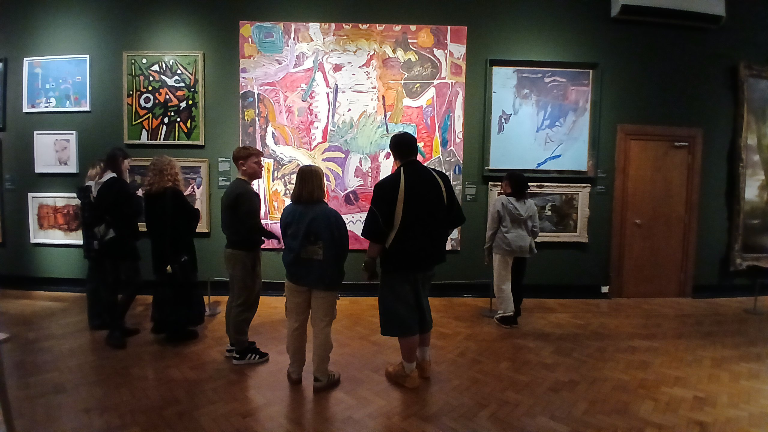 L-INK, a group of young people, are looking at artwork in a gallery setting.