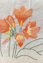 Orange, yellow and green embroidered flowers on pale fabric background 